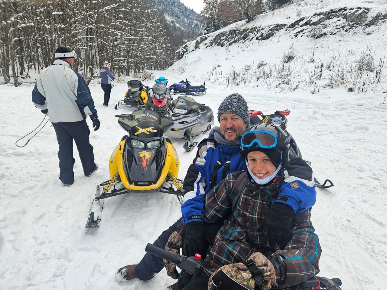 Guests beside snowmobiles on a snowy mountain outing.
