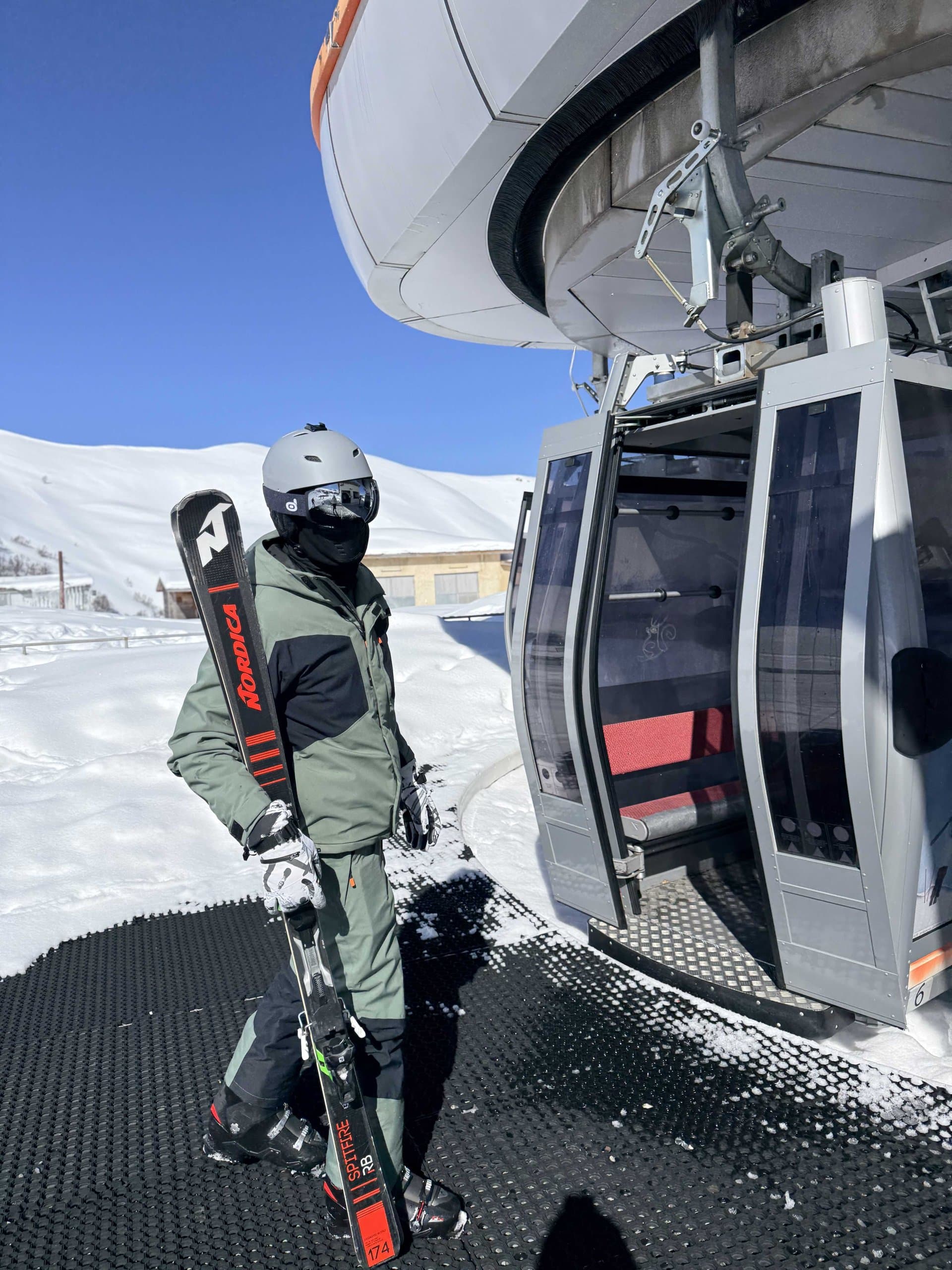 Skier beside a gondola cabin at a mountain lift.