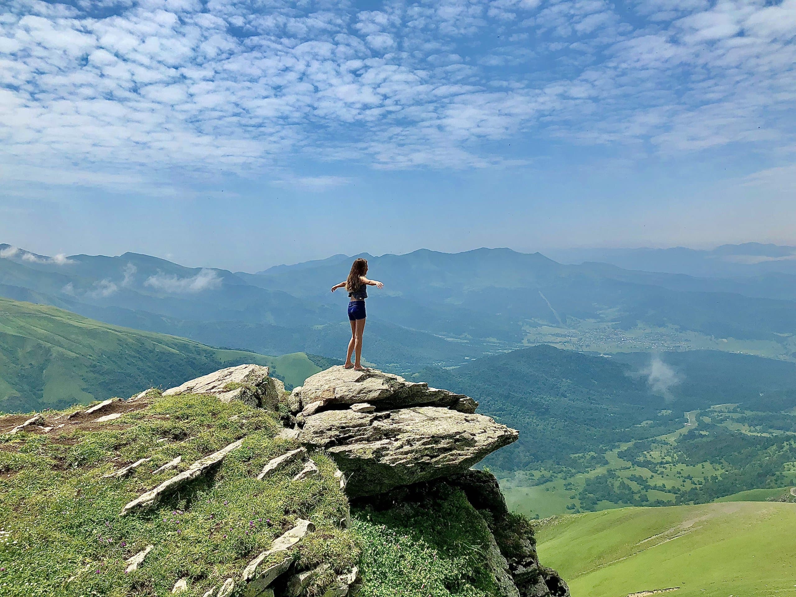 Traveller standing on a rocky viewpoint above green mountains.